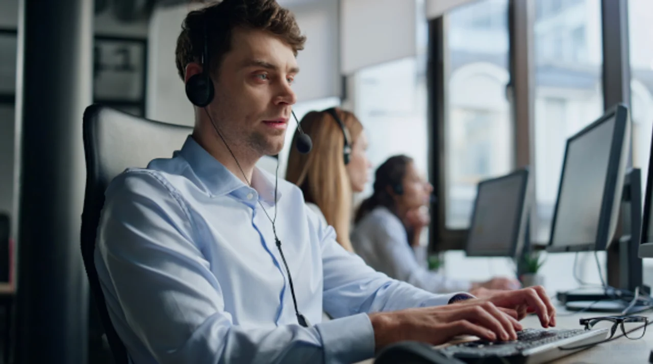 Ein seitlich sichtbarer, an einem Schreibtisch sitzender Mann mit Headset, der auf seinem PC tippt.