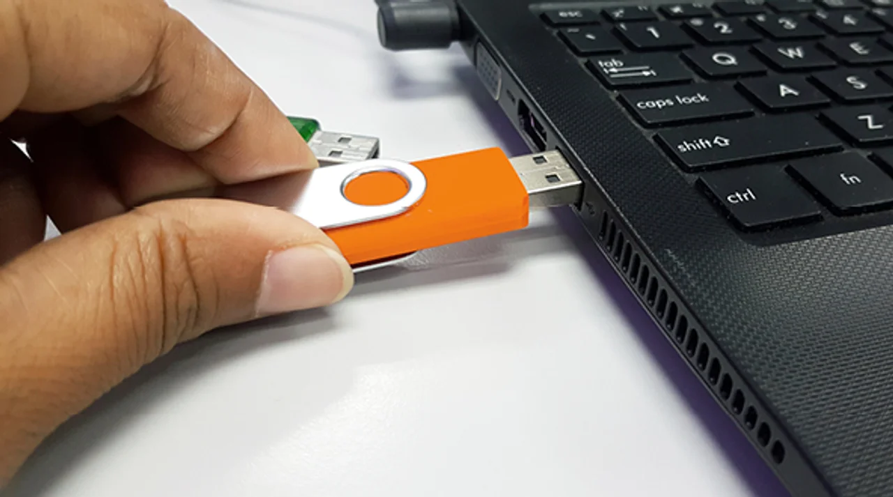 Hand steckt einen USB-Stick seitlich in einen Laptop