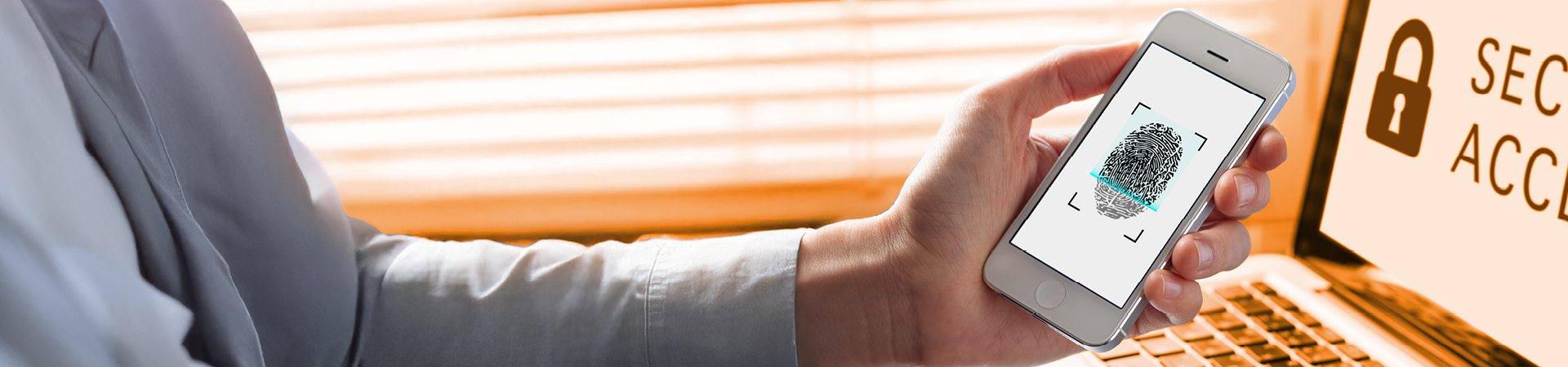 Hand holds up a smartphone in front of a laptop, showing a fingerprint scan.