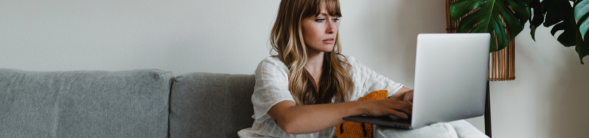 Woman sitting on a sofa with a laptop on the armrest, typing on it