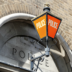 Eine traditionelle Stra&szlig;enlaterne am T&uuml;rbogen einer Polizeistation, auf deren Seiten &bdquo;Police&ldquo; steht 