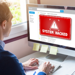 Person betrachtet einen Computerbildschirm mit der Warnung &bdquo;System gehackt&ldquo;