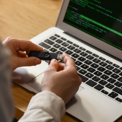 Person verbindet ein USB-Gerät mit einem Laptop, auf dem Quellcode angezeigt wird